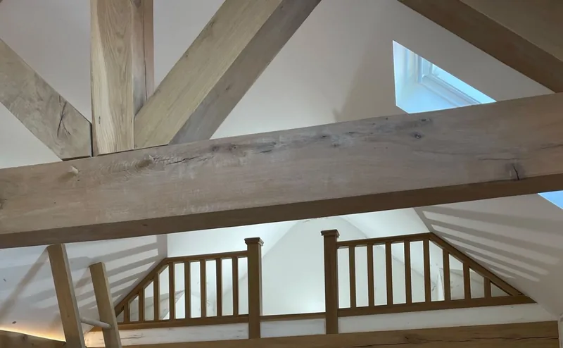 Vaulted ceiling with exposed oak beams and rafters, skylights and an oak mezzanine balustrade above a freshly painted white room
